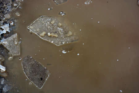 Broken transparent ice, small pieces of ice crust lie near a frozen puddle and float in the water. Spring is warming, the ice is melting on the street.の写真素材