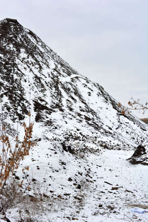 Bright, colorful high mountains, peaks, steep hills are located along the road and covered with light white snow in winter. A very interesting and bewitching landscape against a gray-white sky.の写真素材