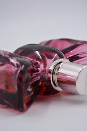 A beautiful red, cherry, plum bottle of women's perfume in the form of a bow with a cherry sweet aroma is located on a white background.の写真素材