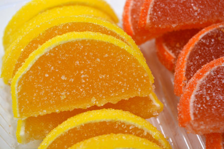 Yellow and orange jelly sweets made of sliced orange slices, lemon, fruits located in plastic transparent containers and sprinkled with sugar.の写真素材