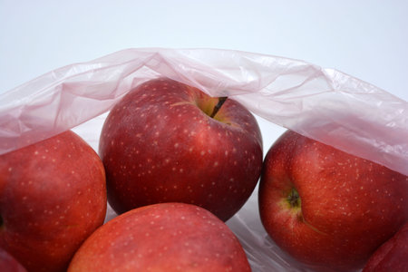 A large package of fruit, healthy food, a lot of red, ripe apples lie in a pink disposable bag. Red apples in a plastic bag on a white background, close-upの写真素材
