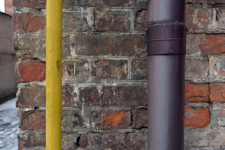 An old red shabby wall with a large plastic purple pipe and a thin yellow pipe. Pipe and yellow pipe on the background of an old brick wallの写真素材