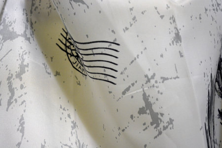 Closeup detail of a piece of white fabric with a pattern on it Unusual textured thin fabric with gray marble, chaotic patterns, gray flowers, postage stamps and inscriptions.の写真素材