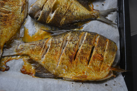 Fried fish on a baking sheet in the oven close-up. Delicious and healthy, baked fish, Carassius with...