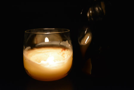Candle in a glass on a black background with copy space. Beautiful glass vessel in the shape of a heart with illumination of fire, candles in the dark.の写真素材