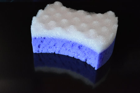 Sponge for washing dishes on a black background, closeup of photo. Clothes, personal care products, purple porous washcloth for the shower is located on a black glossy background.の写真素材