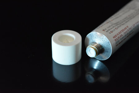 Cosmetics, white anti-inflammation cream in a white metal tube placed on a black glossy background.の写真素材