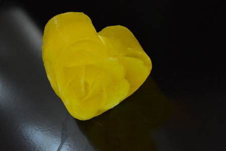 A delicate yellow smelling handmade soap, flowers and rose petals inside in the form of love and heart lies on a black glossy surface with reflection.の写真素材