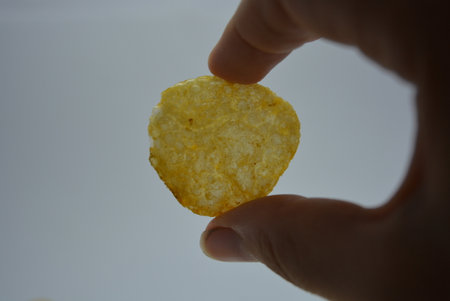 Potato chips in hand on a white background. Selective focus. Snacks, fast and unhealthy food. Female hand holding salted chips on white background.の写真素材