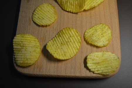 Potato chips on a wooden cutting board. Selective focus. Potatoes fried wavy, embossed, potato chips with sour cream and greens, facies on a wooden board.の写真素材