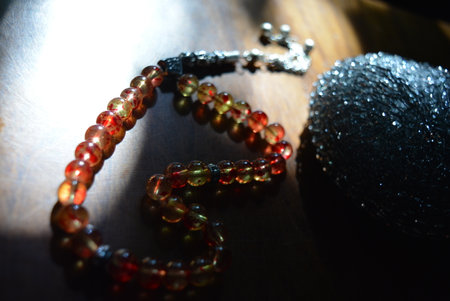 Bracelet made of red and black beads on a wooden. Muslim religious beads, tesbih of yellow and red beads with a metal sponge on a lacquered wooden table lit by the rays of the sun.の写真素材