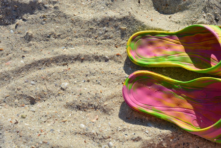 Pink women's slippers with green and yellow divorces on yellow sand with shallow seashell beach of...