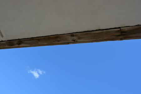 Dark blue sky with white clouds, the top of a tree, a white cement roof and a wooden beam.の写真素材