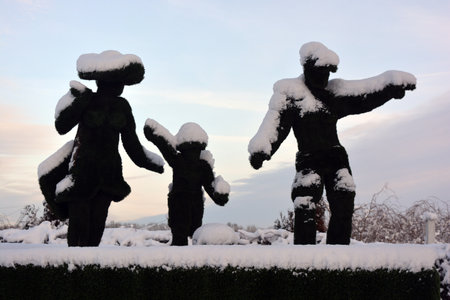 Beautiful architectural monuments, sculptures made from a green mesh in the form of a statue of a woman, a man and a child covered with white snow in winter.の写真素材