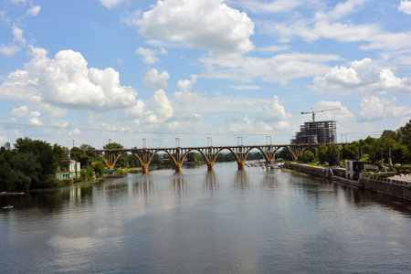 Beautiful view of wide, long blue Dnipro River. Landscapes, gray brick embankment with green trees, new construction sites and bridge in city Dnipro.の写真素材