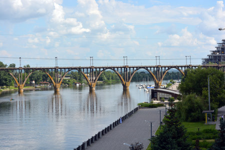 Beautiful view of wide, long blue Dnipro River. Landscapes, gray brick embankment with green trees, new construction sites and bridge in city Dnipro.の写真素材