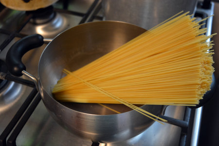 Long Italian durum wheat vermicelli is boiled with hot water in a gray metal saucepan on a gas stove.の写真素材