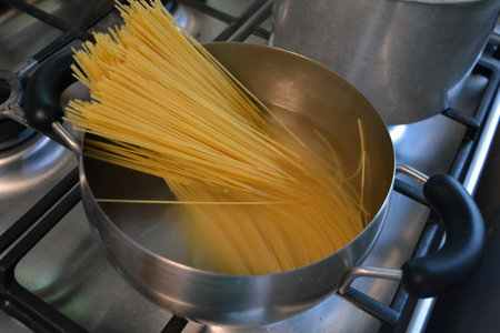 Cooking spaghetti in a pot on a gas stove close-up. Long Italian durum wheat vermicelli is boiled with hot water in a gray metal saucepan on a gas stove.の写真素材
