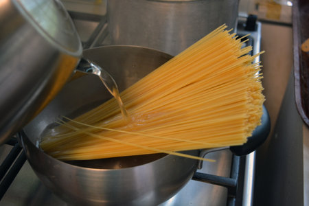 Spaghetti in a saucepan on a stove in a restaurant kitchen. Long Italian durum wheat vermicelli is boiled with hot water in a gray metal saucepan on a gas stove.の写真素材