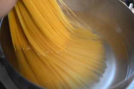 Cooking spaghetti pasta in a saucepan, closeup of photo. Long Italian durum wheat vermicelli is boiled with hot water in a gray metal saucepan on a gas stove.の写真素材