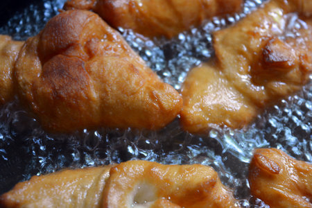 Fried croissants in a frying pan, close-up. Ukrainian national cuisine, fried verguntsi in hot sunflower oil in a black metal frying pan.の写真素材