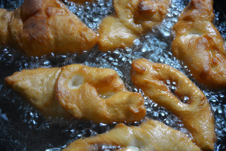 Deep-fried dough stick in a hot pan. Close up. Fried verguntsi in hot sunflower oil in a black metal frying pan.の写真素材