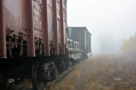 Wagons on the railroad in the foggy autumn morning. Sand paths along the railway, metal rails with a...