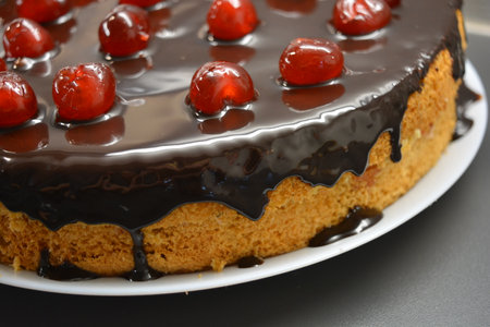 Chocolate cake with cherries on a white plate close-up. White sponge cake "Drunken Cherry" decorated with chocolate icing with caramelized, red, bright, sweet cherries.の写真素材
