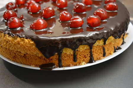Chocolate cake with cherries on a white plate, closeup. White sponge cake Drunken Cherry decorated...