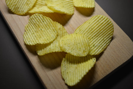 Crispy potato chips on a wooden board. Toned. Thin slices of potatoes, corrugated chips are located...