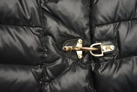 Close up of a zipper on a black jacket with a chain. Beautiful stylish black women short down jacket with white fluffy puffer jacket hanging on gray stone background.の写真素材