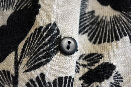 Close up of a button on a woolen sweater with floral print. Black glossy buttons sewn with black...