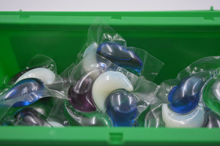 Laundry detergent pods in plastic packaging, showing various blue and white capsules inside a green...