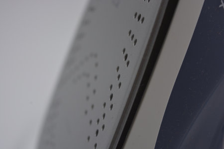 Close-up of a blue iron on a gray background. Selective focus. Gray white plastic iron with sprayer, metal bottom is located on a white plastic background.の写真素材