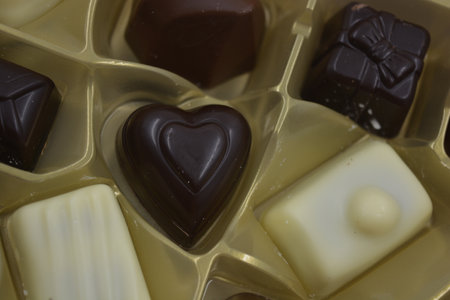 Box of chocolates in the form of hearts. Selective focus. Large delicious candies with different fillings are arranged in gold plastic packaging.の写真素材