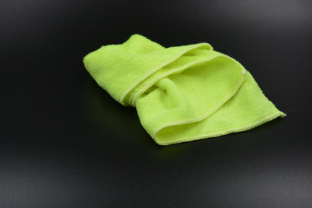 Green microfiber cloth on a black background. Cleaning concept. Bright lemon, yellow cloth, napkin,...