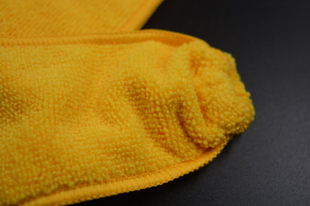 Yellow microfiber cloth on a black background. Close-up. An unusual cleaning cloth, a long yellow microfiber set on a black, matte plastic background.の写真素材
