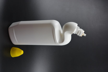 White plastic bottle of shampoo or conditioner with yellow cap on black background. A white plastic bottle with a curved neck and a yellow cap is placed on a black background.の写真素材