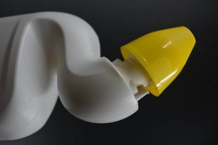 Plastic bottle of toothpaste on a black background close-up. A white plastic bottle with a curved neck and a yellow cap is placed on a black plastic background.の写真素材