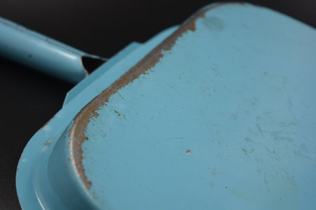 Close up of a blue dustpan isolated on a black background. A blue metal scoop from which the paint has come off is located on a black matte background.の写真素材