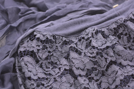 Close up of black lace fabric texture background. Selective focus. Unusual fabrics, crumpled thin dark blue cotton, viscose with beautiful lace with flowers is on a white.の写真素材