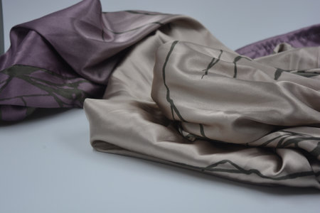 Lilac silk fabric on a gray background. Studio shot. Beige, sand, delicate purple, thin synthetic, silk fabric with dark eyelids, lines are on a white.の写真素材