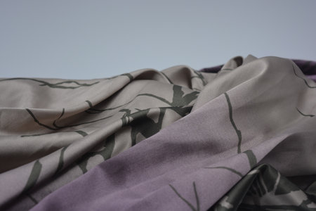 Silk fabric, gray and purple colors, with a print of green leaves. Background texture, pattern.の写真素材