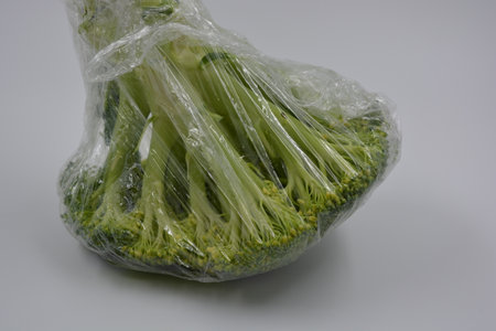 Broccoli in a plastic bag on a gray background. Close up. Cabbage, green healthy broccoli wrapped in cling film and placed on a white matte background.の写真素材
