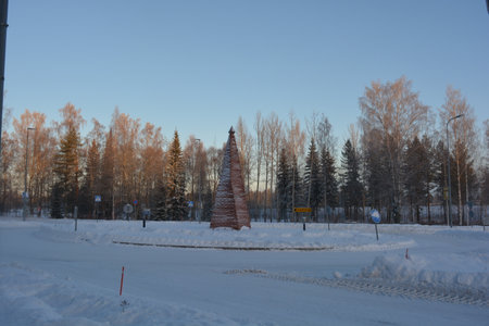 Winter landscape with trees in the snow and the road in the city. The monument of a New Year's tree, a Christmas tree made of wooden sticks, is made in an unusual and unique way.の写真素材