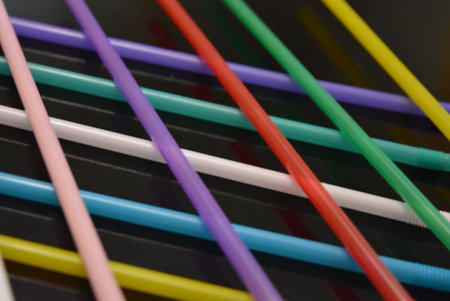 Colored drinking straws on a black background, close-up. Many red, white, blue, green, purple, pink,...