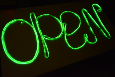 Word open in green neon light on a black background close-up. Beautiful thin glowing green, lime wires, beaten cable twisted in the form of a sign OPEN on a black plastic.の写真素材