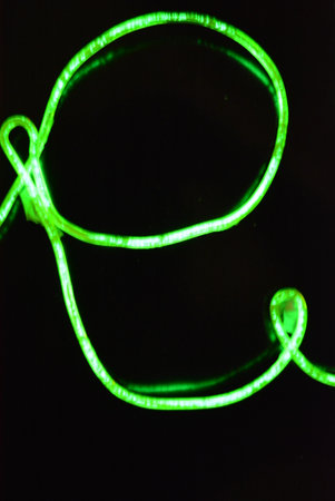 Neon lights. Abstract background with green neon lights. Beautiful thin glowing green, lime wires, beaten cable twisted in the form of a sign on a black plastic.の写真素材