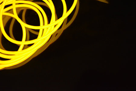 Yellow neon lights on a black background, close-up, abstract. Beautiful thick yellow, orange wires are chaotically located and twisted on a black plastic.の写真素材