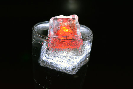 Candle light in a glass with water drops on a black background. Transparent glowing cubes of white...